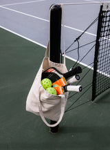 Tote bag hanging on a tennis court net post, filled with Sunii Energy Gum packs, tennis paddles, and balls